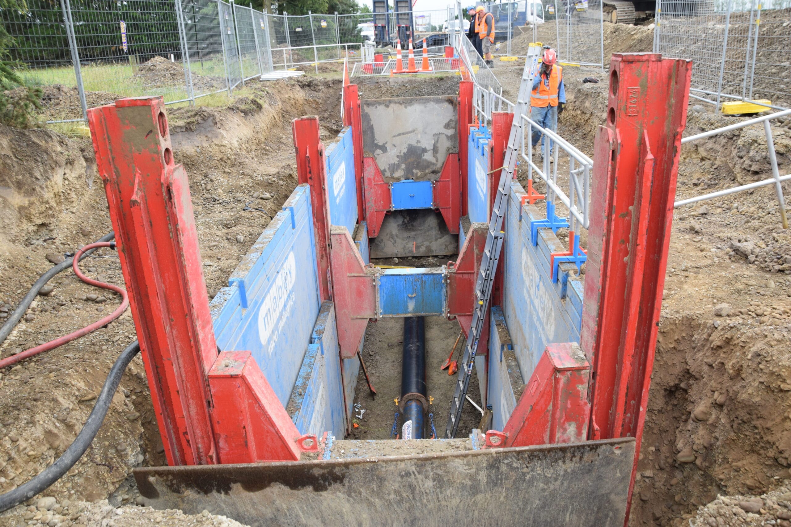 Excavated trench with Mabey hydraulic vertical shoring and underground pipe installation in progress