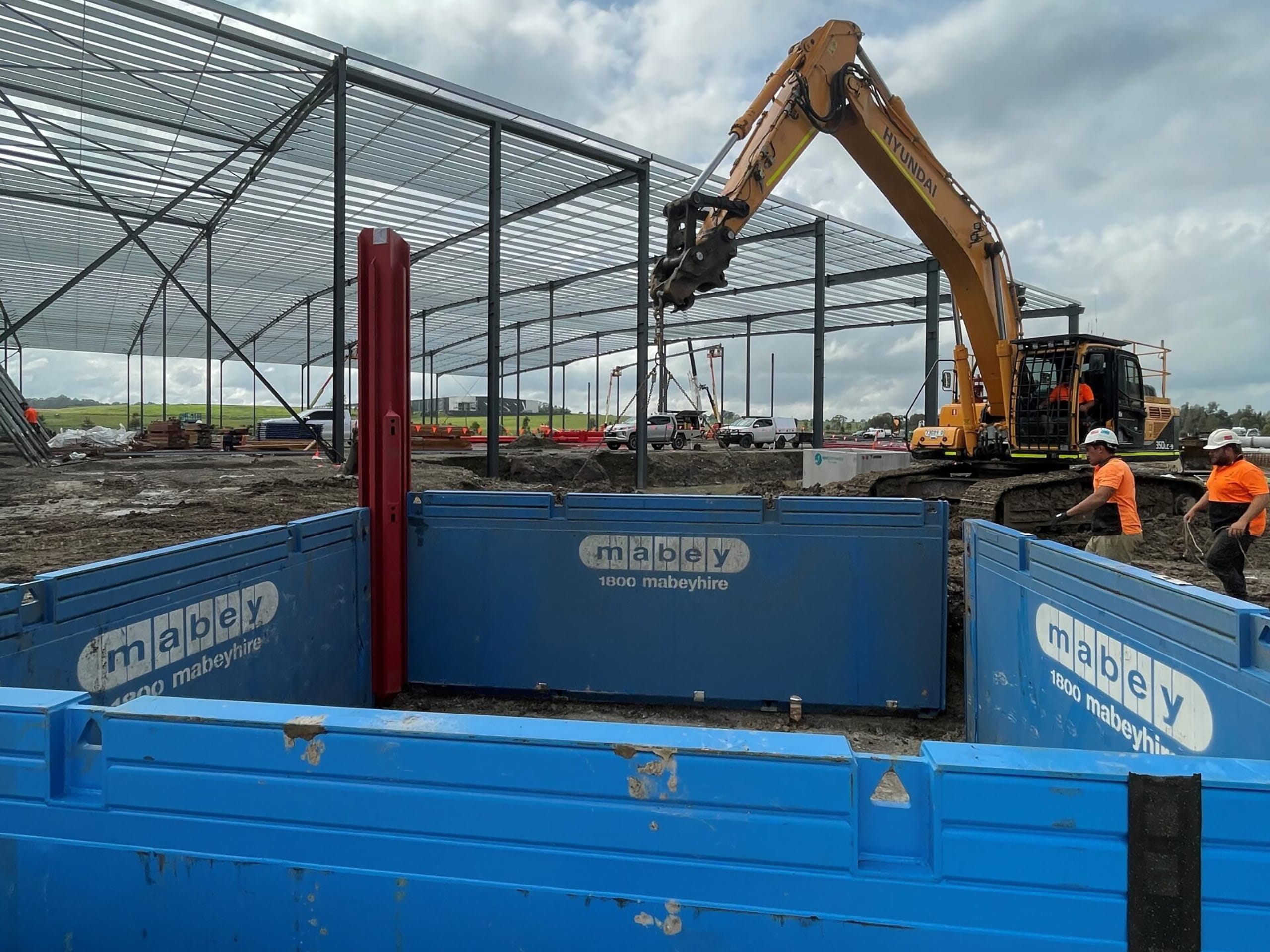 Crew and excavator installing Mabey trench shoring shield for safe excavation