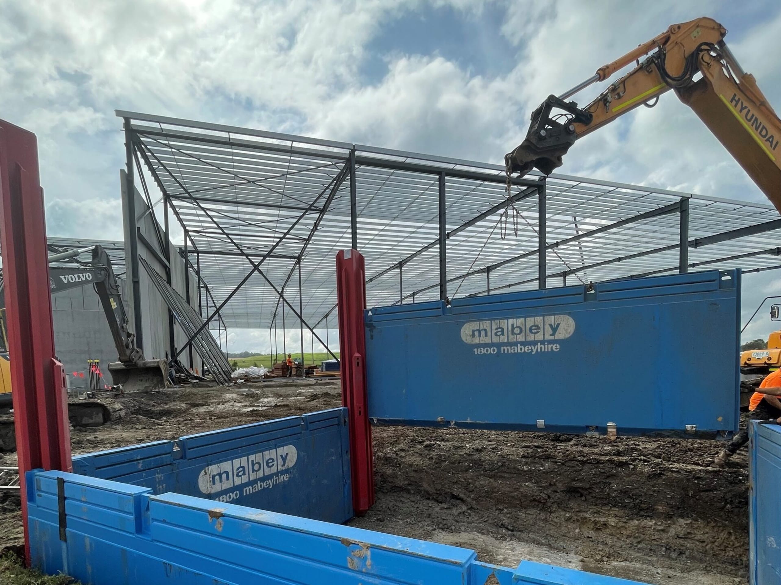 Excavator placing Mabey trench shoring shield at building site excavation